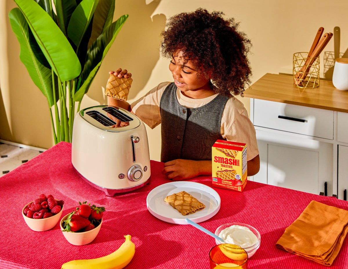 Child at a toaster with a box of Smash Toasties